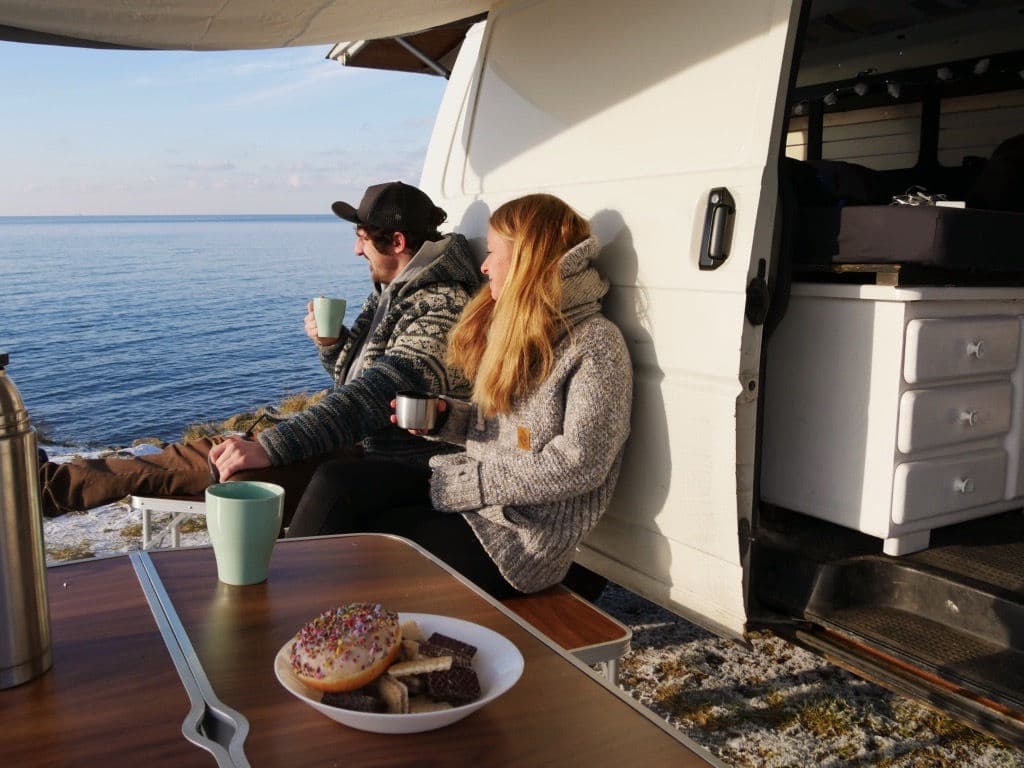 Gedeckter Campingtisch mit Kaffee am Meer neben dem Van